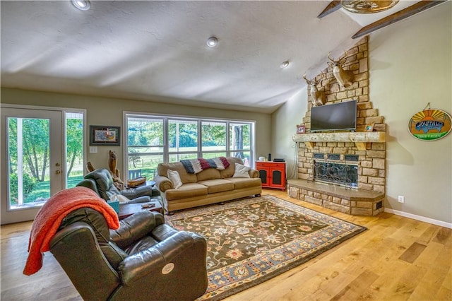 living room featuring wood finished floors, baseboards, a stone fireplace, and vaulted ceiling