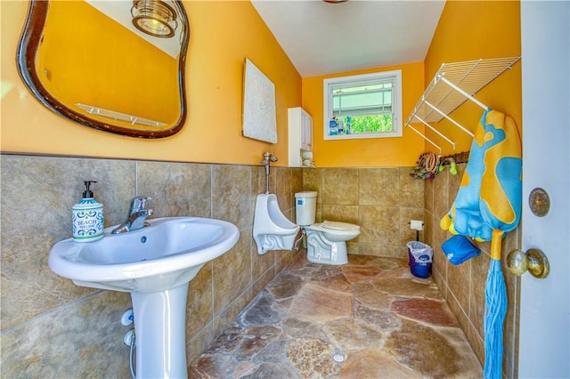 full bathroom featuring a shower with shower curtain, toilet, stone finish floor, wainscoting, and tile walls