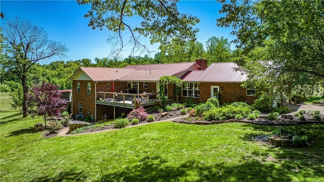 rear view of property with metal roof, a deck, a chimney, and a lawn