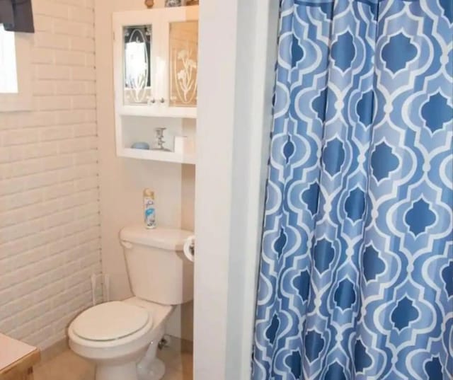 bathroom featuring toilet, brick wall, and a shower with curtain