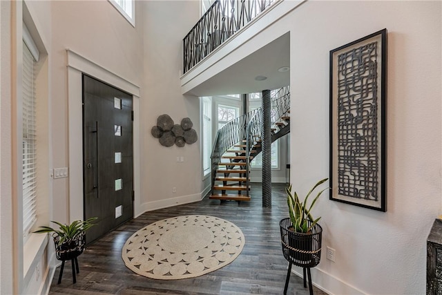 foyer entrance featuring baseboards, a towering ceiling, wood finished floors, and stairs