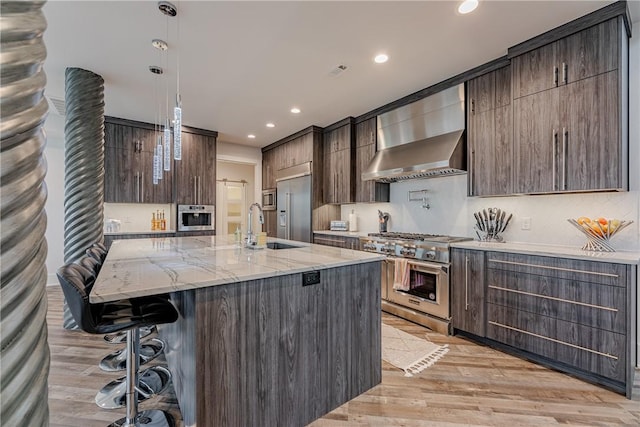 kitchen with wall chimney exhaust hood, modern cabinets, a kitchen bar, light wood-type flooring, and high quality appliances
