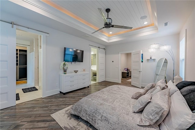 bedroom featuring baseboards, dark wood-type flooring, a barn door, visible vents, and a tray ceiling