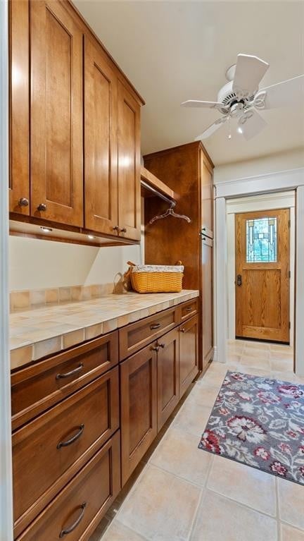 kitchen with brown cabinetry, light tile patterned flooring, wooden counters, and a ceiling fan