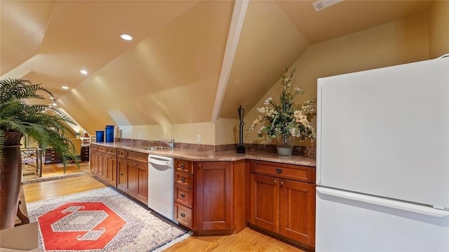 kitchen featuring white appliances, lofted ceiling, light wood-style flooring, brown cabinets, and a sink