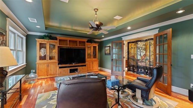 living area featuring crown molding, a tray ceiling, french doors, wood finished floors, and baseboards