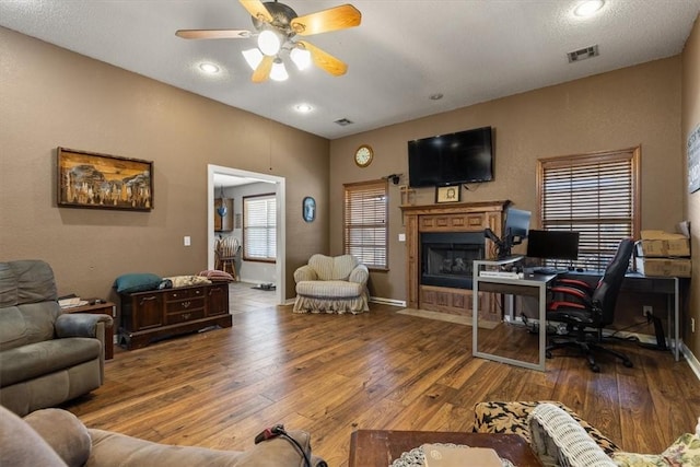 living area featuring baseboards, a ceiling fan, a fireplace with flush hearth, visible vents, and hardwood / wood-style flooring