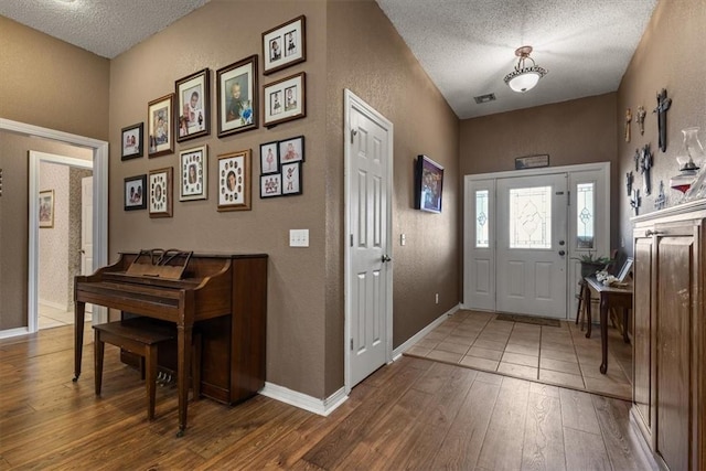 foyer entrance featuring a textured ceiling, a textured wall, wood-type flooring, and baseboards