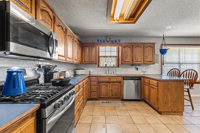 kitchen featuring stainless steel appliances, a peninsula, brown cabinetry, and a sink