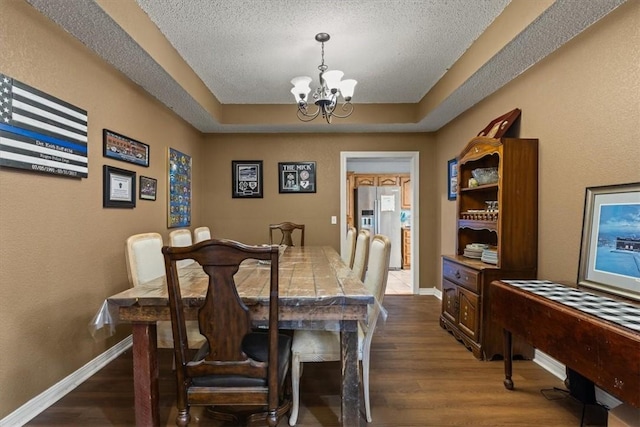 dining room with a raised ceiling, a textured ceiling, dark wood-style flooring, and a notable chandelier