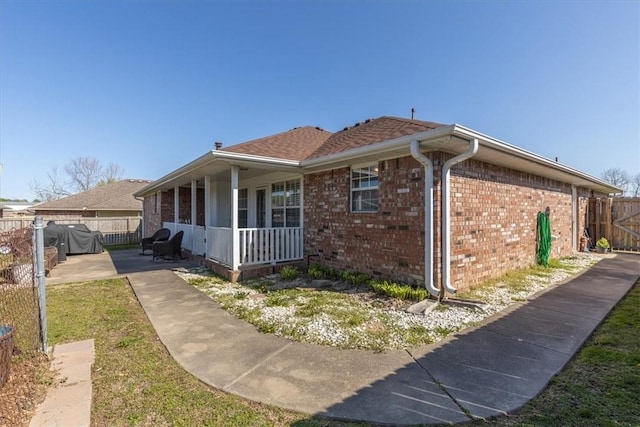 view of side of home featuring a patio, brick siding, fence, and covered porch