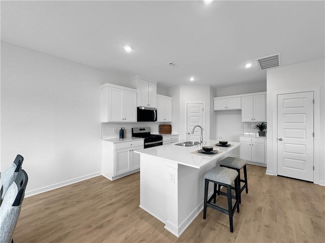 1963 Larkspur St, Springdale, AR 72762 - kitchen with stainless steel microwave, range, light wood-style floors, a center island with sink, and recessed lighting