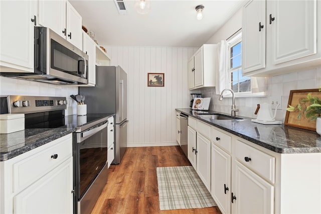 kitchen featuring white cabinets, visible vents, stainless steel appliances, a sink, and wood finished floors