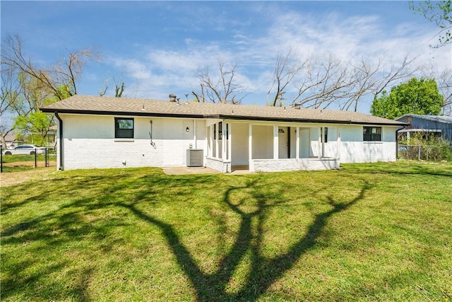 rear view of property with central AC, fence, and a lawn