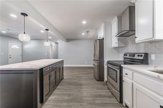 kitchen with white cabinets, appliances with stainless steel finishes, a center island, and wall chimney exhaust hood