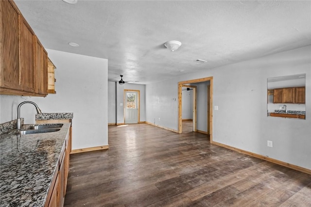 kitchen with dark stone countertops, a sink, brown cabinets, baseboards, and dark wood-style floors