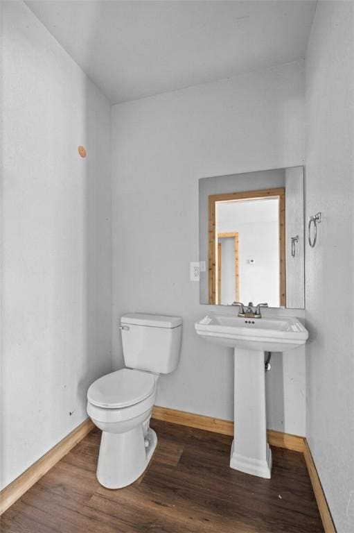 half bathroom with baseboards, toilet, and wood finished floors