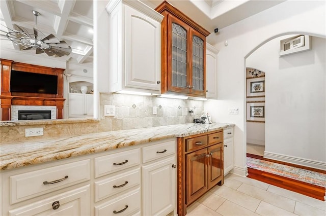kitchen with tasteful backsplash, glass insert cabinets, arched walkways, and light stone counters