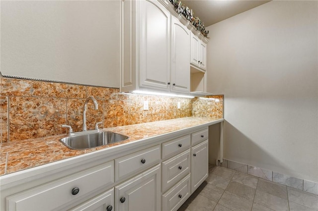 kitchen with white cabinetry, light countertops, a sink, decorative backsplash, and baseboards