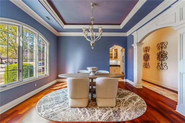 dining area featuring arched walkways, a chandelier, a tray ceiling, ornate columns, and wood finished floors