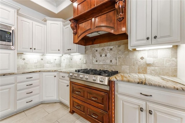 kitchen with custom exhaust hood, tasteful backsplash, light tile patterned floors, white cabinets, and stainless steel appliances