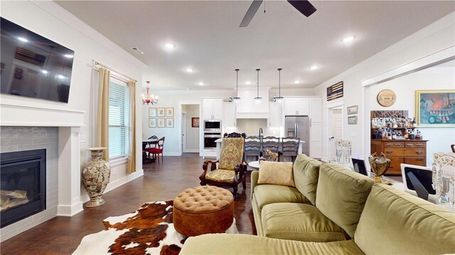 living room featuring visible vents, a glass covered fireplace, dark wood-style floors, recessed lighting, and ceiling fan with notable chandelier