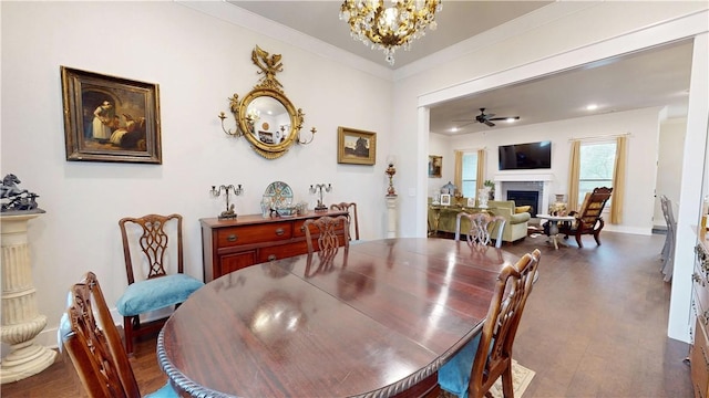 dining area featuring a fireplace, dark wood finished floors, baseboards, ceiling fan with notable chandelier, and ornamental molding