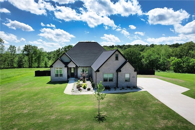 view of front of home with brick siding, a front lawn, driveway, and a forest view