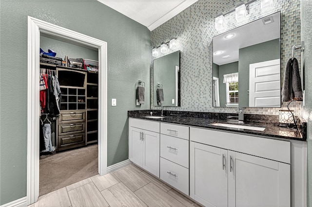 bathroom with a sink, double vanity, a walk in closet, and crown molding