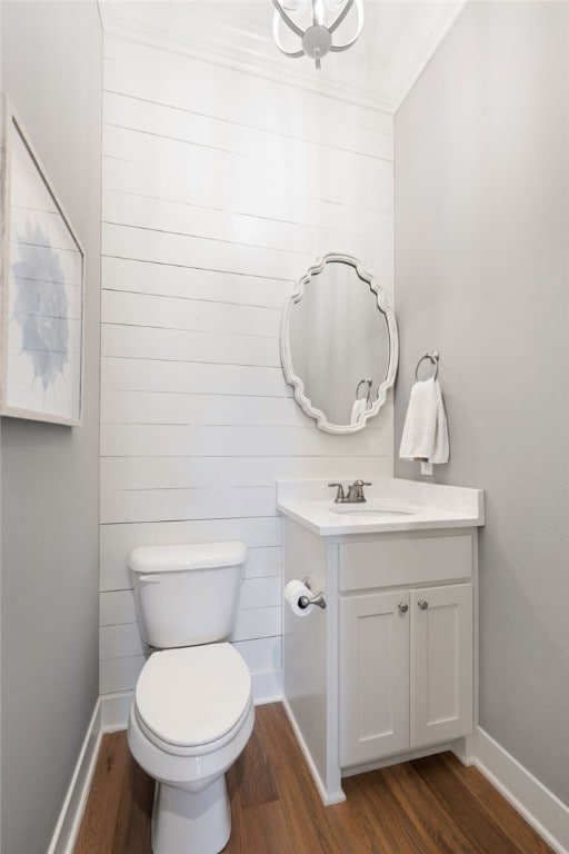 half bathroom featuring baseboards, toilet, crown molding, vanity, and wood finished floors