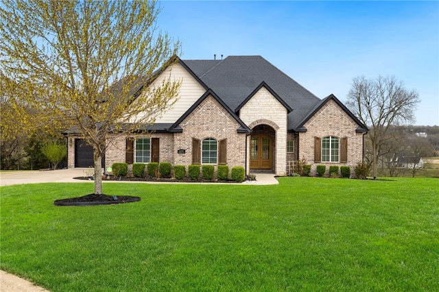 french country inspired facade with concrete driveway, a front yard, brick siding, and french doors