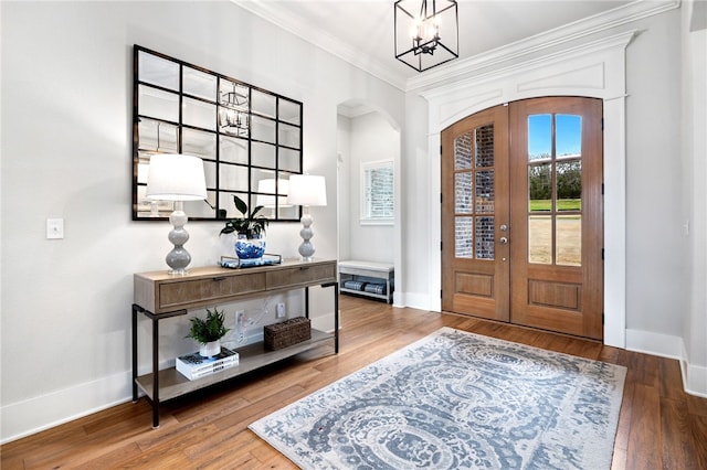 foyer entrance featuring crown molding, arched walkways, wood finished floors, french doors, and a notable chandelier