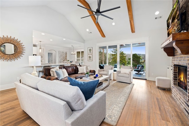 living room featuring light wood-type flooring, a ceiling fan, visible vents, a brick fireplace, and high vaulted ceiling