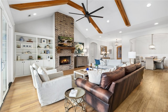 living room with arched walkways, light wood finished floors, a brick fireplace, and ceiling fan