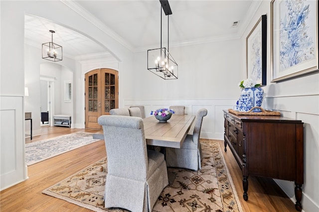 dining area with arched walkways, a chandelier, crown molding, wood finished floors, and french doors