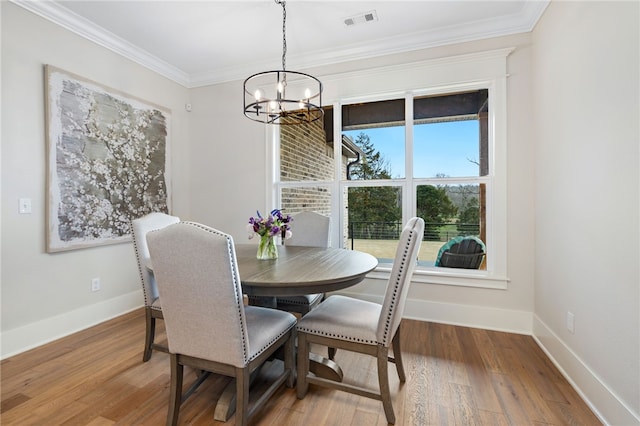 dining space featuring crown molding, an inviting chandelier, visible vents, wood finished floors, and baseboards