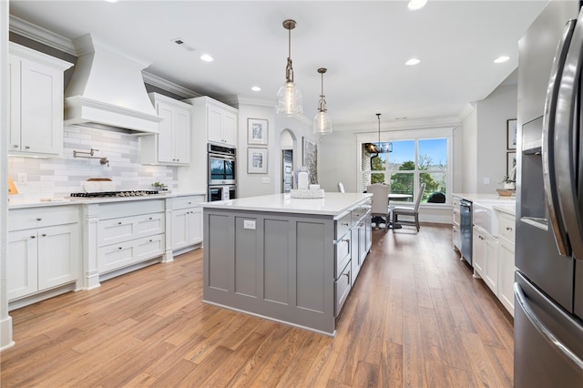 kitchen with custom exhaust hood, ornamental molding, light countertops, white cabinets, and appliances with stainless steel finishes