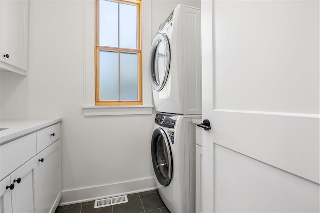 laundry room with visible vents, stacked washer / dryer, dark tile patterned floors, baseboards, and cabinet space