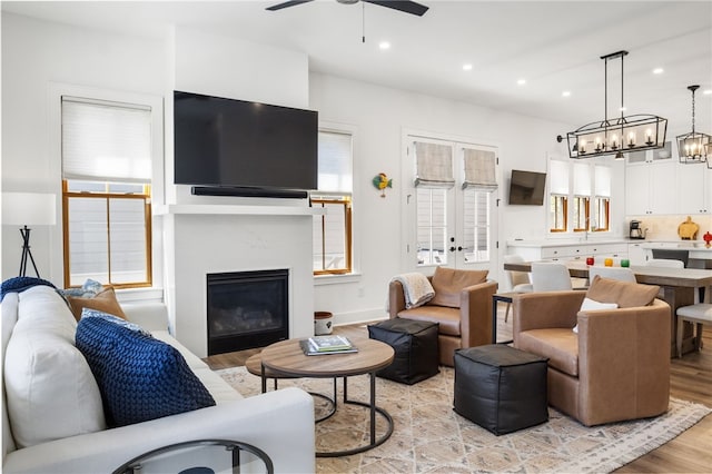 living room featuring light wood-style floors, ceiling fan with notable chandelier, a glass covered fireplace, and recessed lighting
