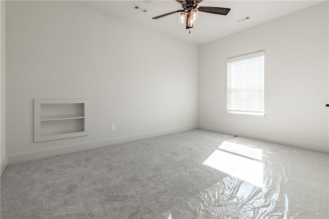 empty room with built in features, carpet floors, ceiling fan, and baseboards