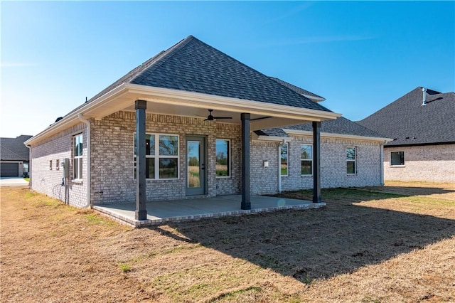 rear view of property featuring ceiling fan, a lawn, brick siding, a patio area, and roof with shingles