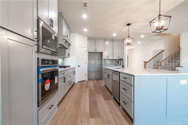 kitchen with stainless steel appliances, a chandelier, light wood-type flooring, a sink, and light countertops