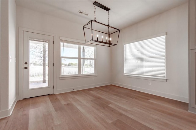 unfurnished dining area featuring a chandelier, plenty of natural light, light wood-style floors, and baseboards