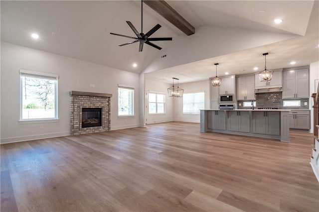 unfurnished living room featuring beam ceiling, recessed lighting, ceiling fan, light wood-type flooring, and a brick fireplace