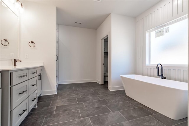 full bath with vanity, a freestanding tub, toilet, and baseboards