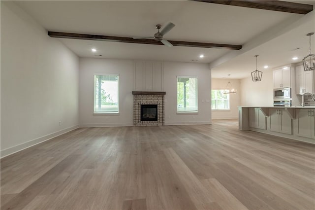 unfurnished living room featuring a chandelier, a ceiling fan, beamed ceiling, baseboards, and light wood-type flooring