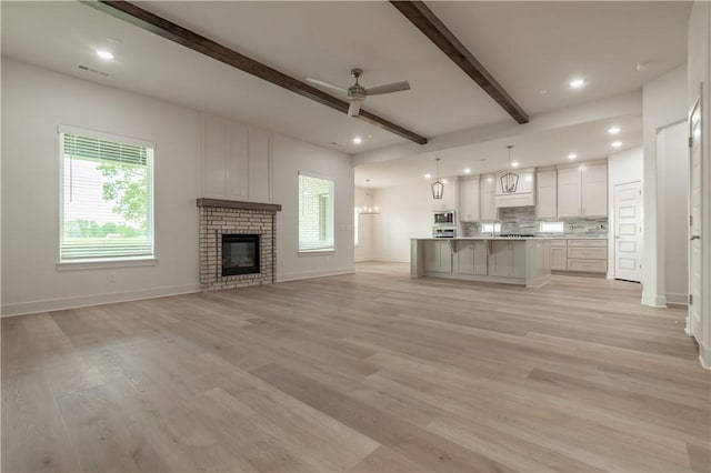 unfurnished living room with ceiling fan, beamed ceiling, baseboards, a brick fireplace, and recessed lighting