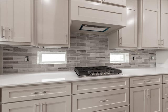 kitchen with light countertops, backsplash, stainless steel gas cooktop, and white cabinets