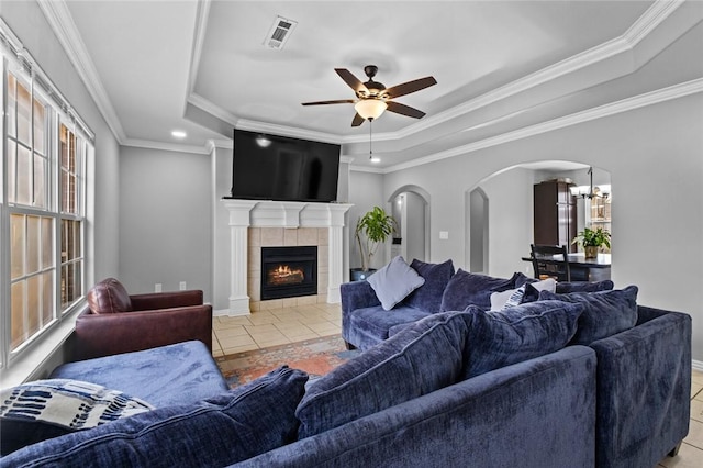 living room with a fireplace, a ceiling fan, light tile patterned flooring, visible vents, and a tray ceiling