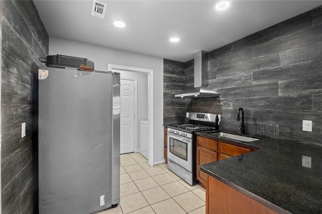 kitchen with light tile patterned floors, wall chimney exhaust hood, dark countertops, a sink, and stainless steel appliances